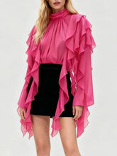 Model wearing a ruffled blouse with layered fringe detailing and a stand collar, styled against a neutral studio background