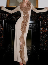 Model wearing a floor-length gown with cascading ruffle detailing, posed elegantly in a formal interior setting