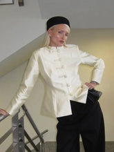 Staircase outfit shot of an ivory satin-look tailored jacket with frog closures, styled with black trousers and a beret for contrast.
