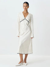 A woman modeling a satin polka dot maxi dress with a V-neckline.