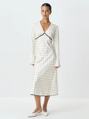 A woman modeling a satin polka dot maxi dress with a V-neckline.