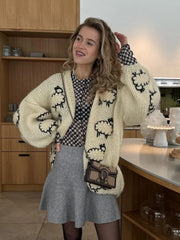 Woman wearing a cream cardigan with black sheep patterns in a kitchen.