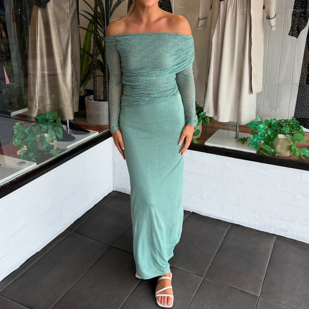 Person wearing a close-up of a teal asymmetric neckline, sheer woven blouse with folded detailing in an indoor setting with plants and clothing in the background.