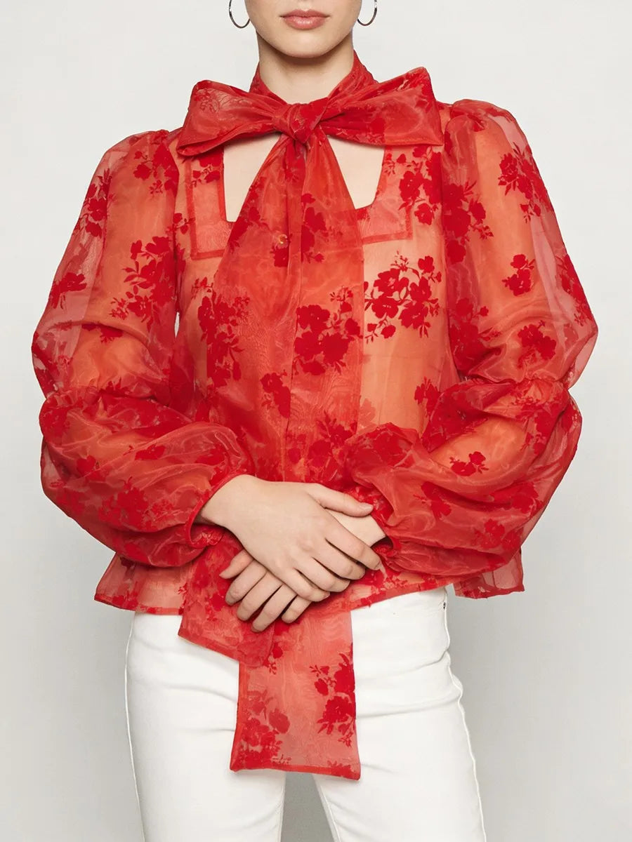 Red sheer blouse with statement bow neckline and lantern sleeves styled over white trousers