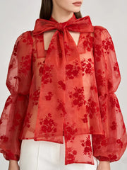 Close-up of bow-neck detail and lightweight sheer woven texture on expressive blouse