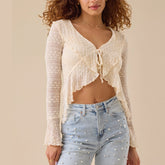 Woman wearing a sheer floral lace bow-tie blouse styled with light denim for summer layering and light blue jeans against a beige background