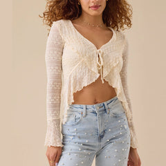 Woman wearing a sheer floral lace bow-tie blouse styled with light denim for summer layering and light blue jeans against a beige background