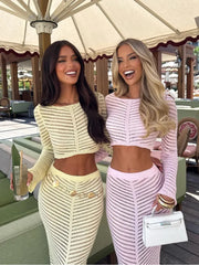 Two women wearing sheer knit co-ord sets with long skirts in an outdoor café