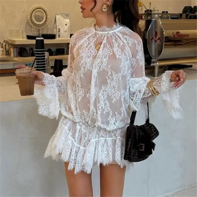 A woman modeling a sheer lace long sleeve mini dress.