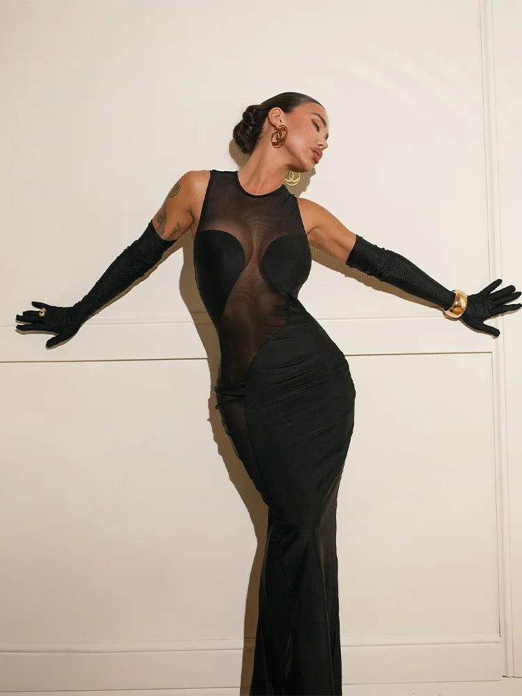 Woman wearing a sleeveless black mesh maxi dress with long gloves against a white background