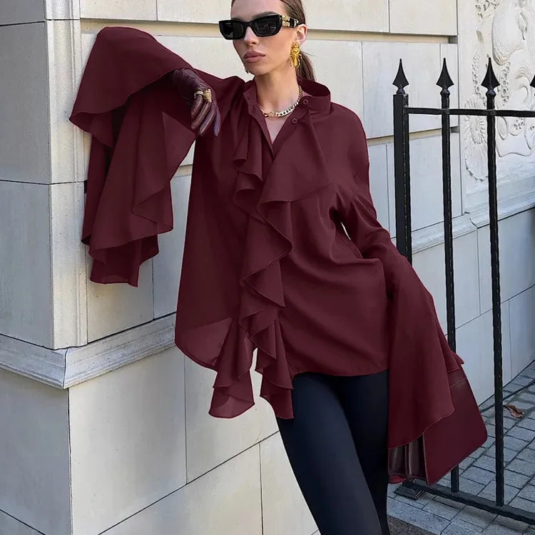 Side view of a Woman wearing a burgundy ruffled top and sunglasses, standing against a building.