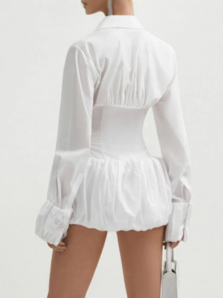 Side back view of a model wearing a long-sleeve shirt dress in white with pleated waist detail on a plain background.