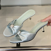 Light blue silk crystal bow slides styled for summer party and brunch on a reflective surface