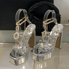 Silver high-heeled sandals with decorative straps on a reflective surface.