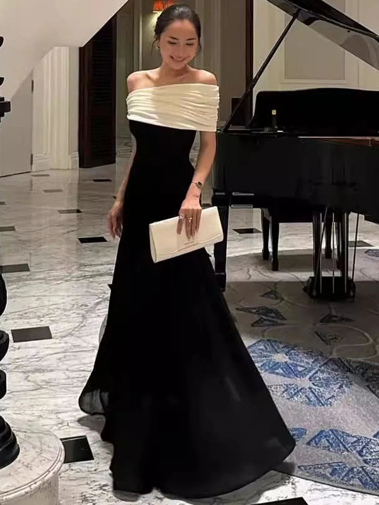 Woman in a black and white evening gown standing in a formal setting with a piano in the background.