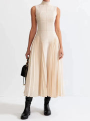Beige sleeveless pleated dress paired with black boots on white background