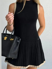 Woman wearing a black dress holding a black handbag against a light gray background