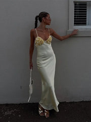 Woman in a white evening gown with floral details against a plain wall.