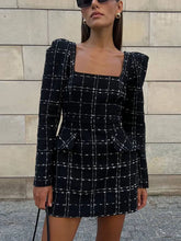 Woman wearing a black and white checkered dress against a stone wall.