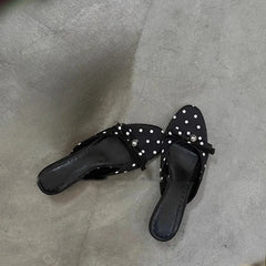 Black sandals with white polka dots and rhinestones on a gray concrete floor.