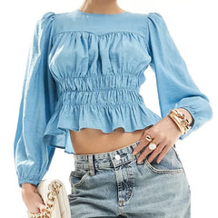 A woman wearing a smocked and ruffled crop top with long sleeves.