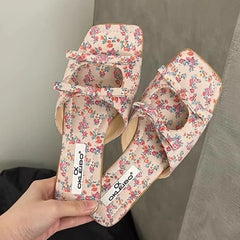 Soft latex summer party slippers for fashionable women’s wear floral patterned sandals held by a hand against a neutral background