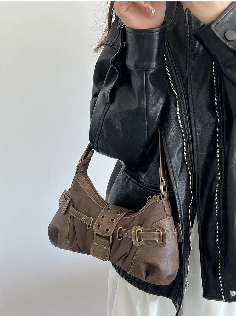 Person wearing a black leather jacket holding a vintage-inspired brown shoulder bag styled for casual and high street fashion against a white background