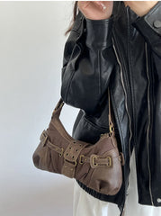 Person wearing a black leather jacket holding a vintage-inspired brown shoulder bag styled for casual and high street fashion against a white background