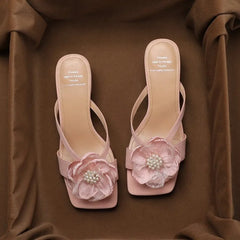 Pink PU sandals featuring pearl flower embellishments for garden weddings. Pair of pink high-heeled sandals with floral decorations on a brown fabric background