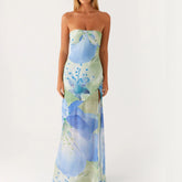 Woman in strapless blue floral maxi dress with side slit standing against white background