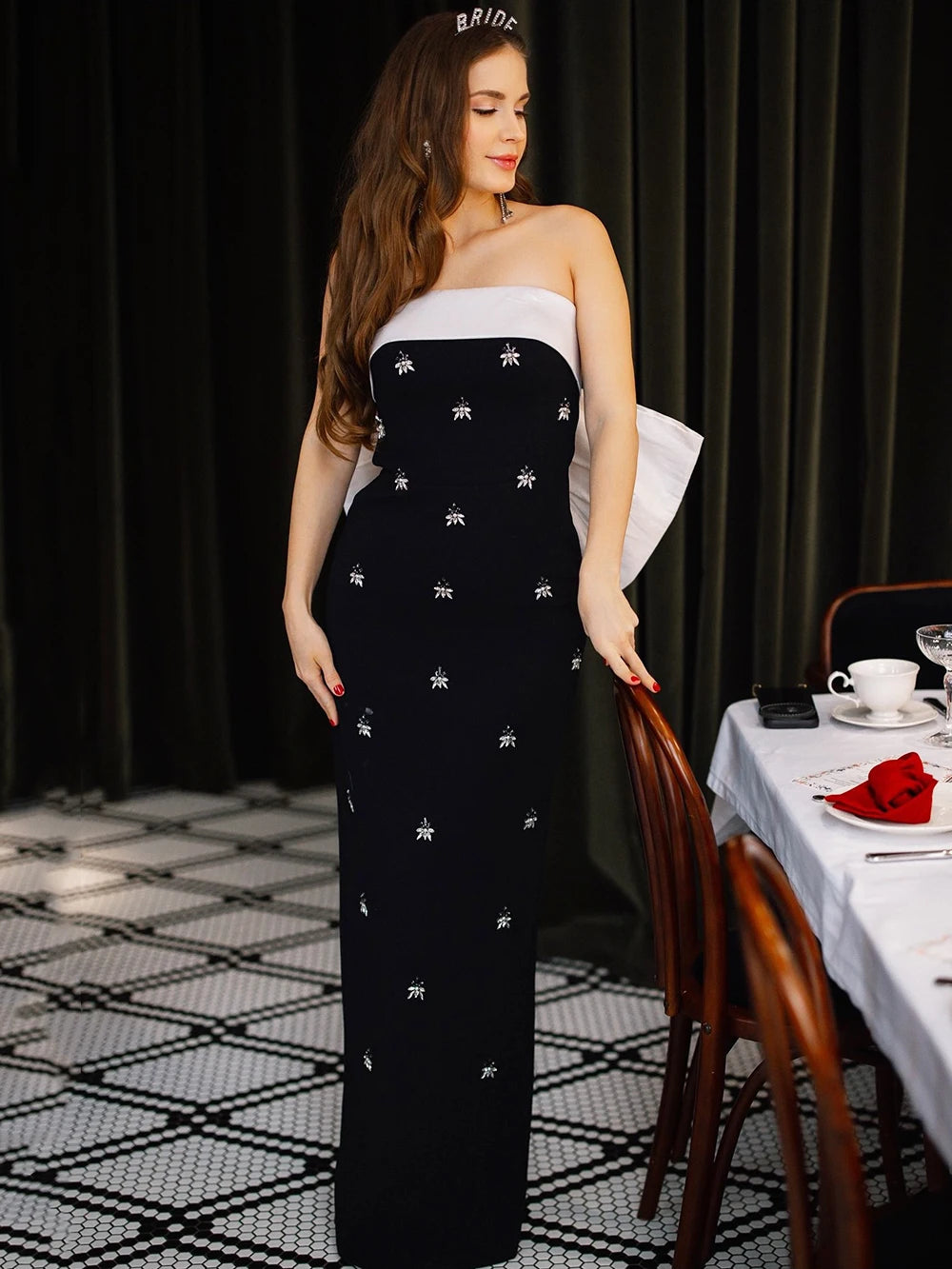 Woman wearing black strapless maxi dress with diamond embellishments in a formal dining setting