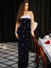 Woman wearing black strapless maxi dress with diamond embellishments in a formal dining setting