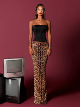 Woman wearing strapless black corset and leopard sequin maxi skirt against studio backdrop