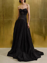 Full-length strapless corset maxi gown with a pleated skirt, styled minimally against a metallic studio wall for a formal silhouette.
