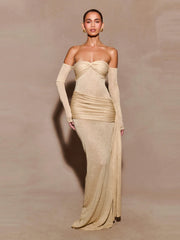 A woman wearing a strapless beige draped evening gown with a sculpted fit on a plain background