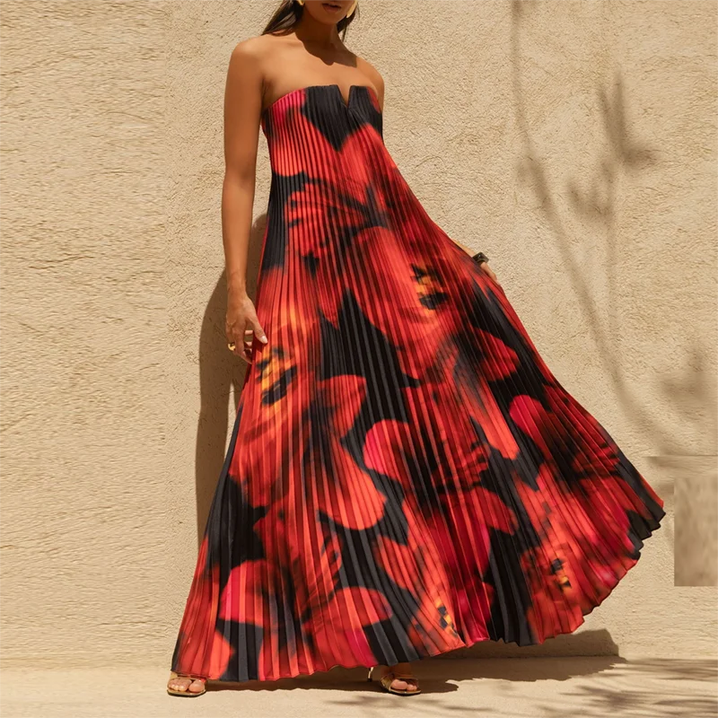 Woman wearing a strapless floral pleated maxi dress with a flowy swing skirt against a beige wall.