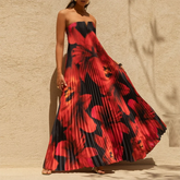 Woman wearing a strapless floral pleated maxi dress with a flowy swing skirt against a beige wall.