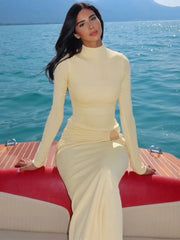 Woman in a yellow dress sitting on a boat with water and mountains in the background
