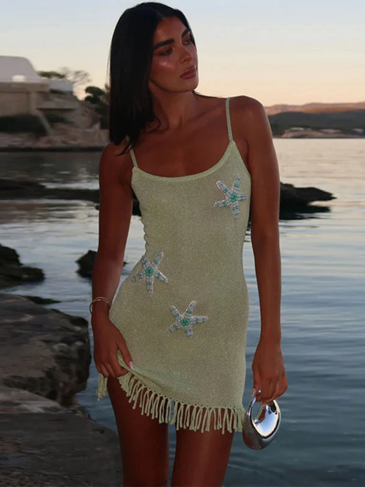 A woman in a green knitted mini dress with tassel hemline standing by a body of water.