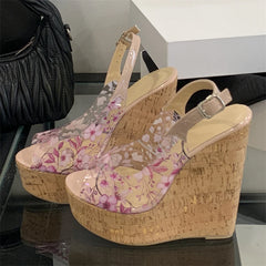 Floral wedge sandals on a reflective surface with a black handbag in the background.