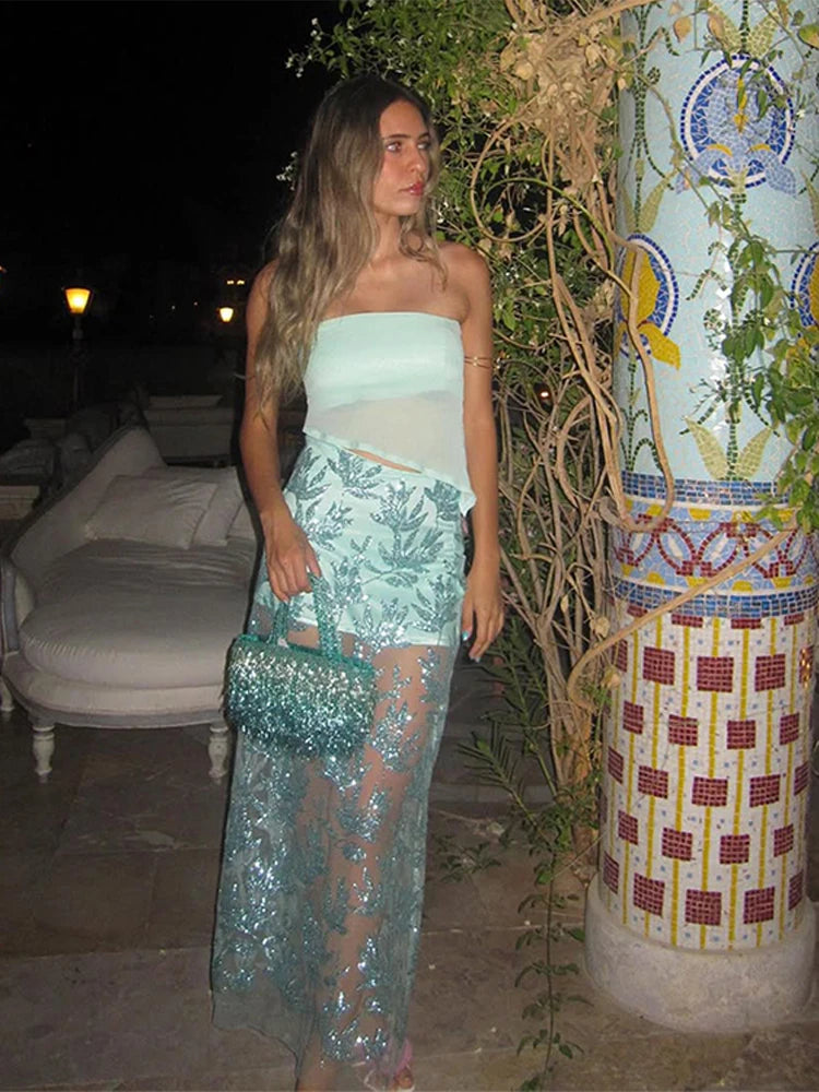 A woman in a Sheer ankle-length skirt and tube top, glowing night, is standing next to a decorative column at night.