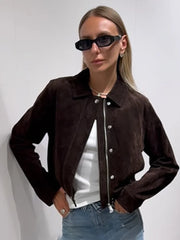 Woman wearing a brown jacket with a white shirt and blue jeans against a plain background