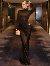 Woman in a long-sleeve turtleneck ruched maxi dress in blackstanding in a modern interior setting.