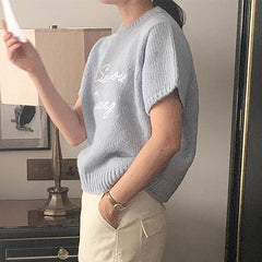 Person wearing a light blue sweater with text, standing indoors.