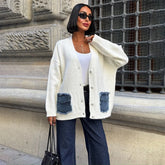 Model wearing a cream V-neck knit cardigan with denim patch pockets, styled with dark wide-leg jeans beside a stone building.