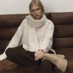 Model wearing a white V-neck scarf detail knit sweater seated indoors on a sofa with a relaxed posture.