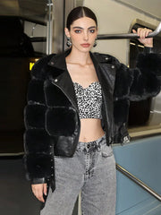 Woman wearing a black fur-trimmed leather jacket, leopard print top, and jeans on a train.