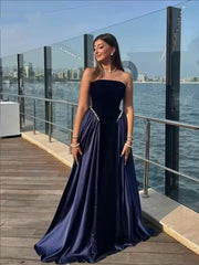 Woman wearing a strapless velvet A-line gown with pearl detail, standing outdoors against waterfront evening light.