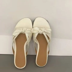 White low-heel slippers styled for women’s office and casual wear. A Pair of white sandals with bow details on a neutral background
