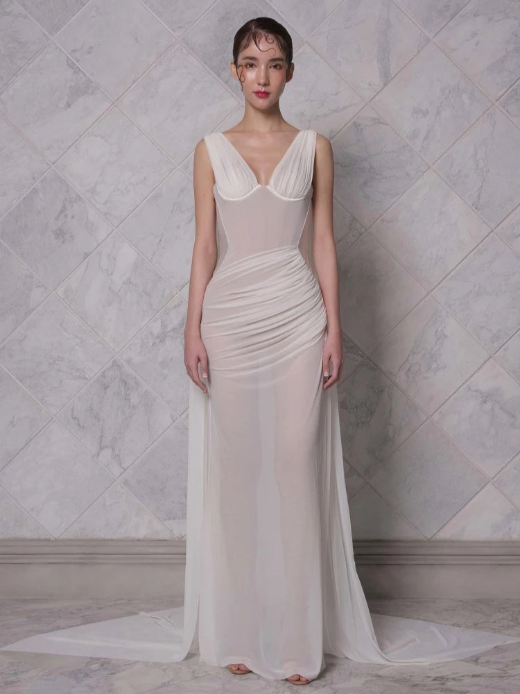 White draped bustier deep v neck maxi dress styled for evening parties. Woman wearing a white evening gown against a marble wall.